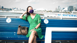 Josee Rose seated on the New York Waterway Ferry, wearing a face covering and a green dress. 